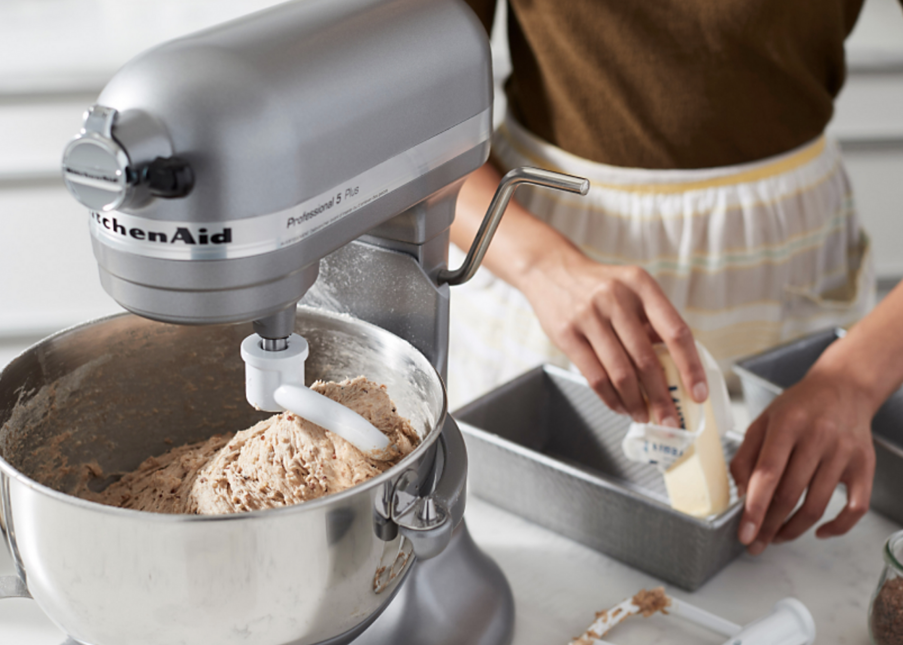 KitchenAid stand mixer mixing dough beside a person placing dough into a loaf pan.