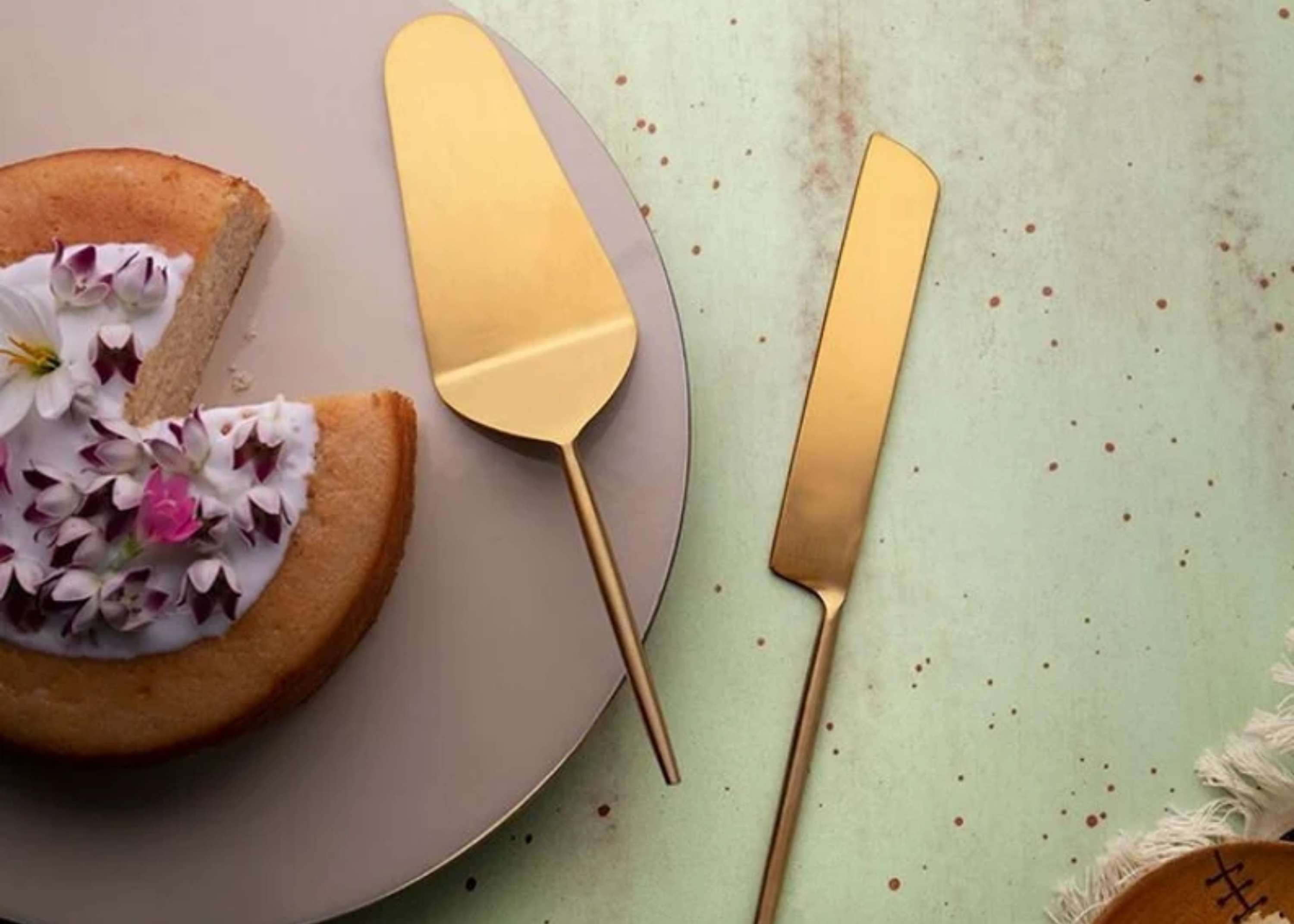 Cake topped with flowers on a plate beside a gold cake server and knife.