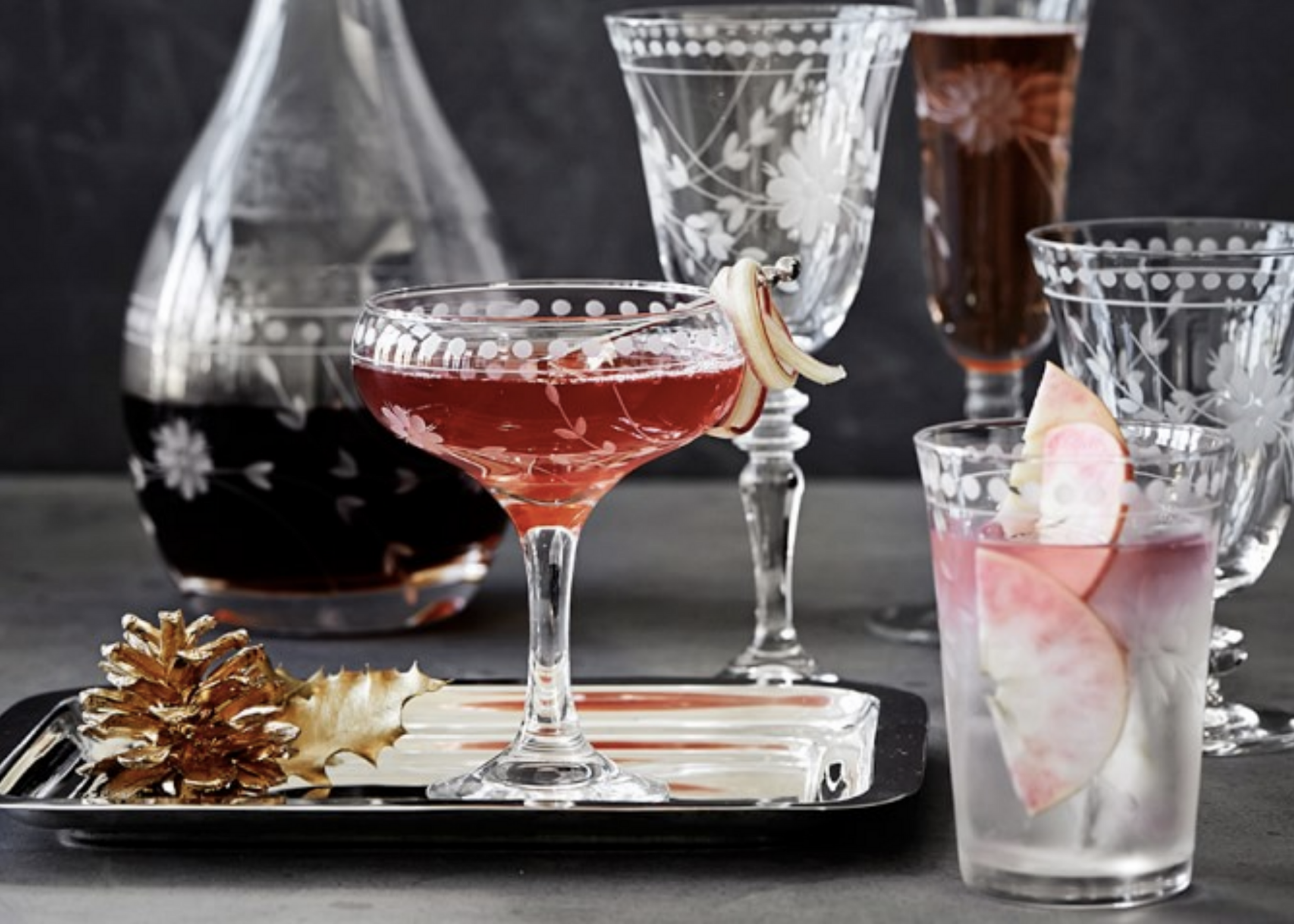 Decorated drinking glasses and a carafe arranged on a tray, with pink and red beverages.