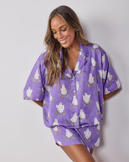 Front three-quarter view of the Eerie Amethyst Gardening Ghosts short pajama set, showing the collared button-down top and matching shorts.