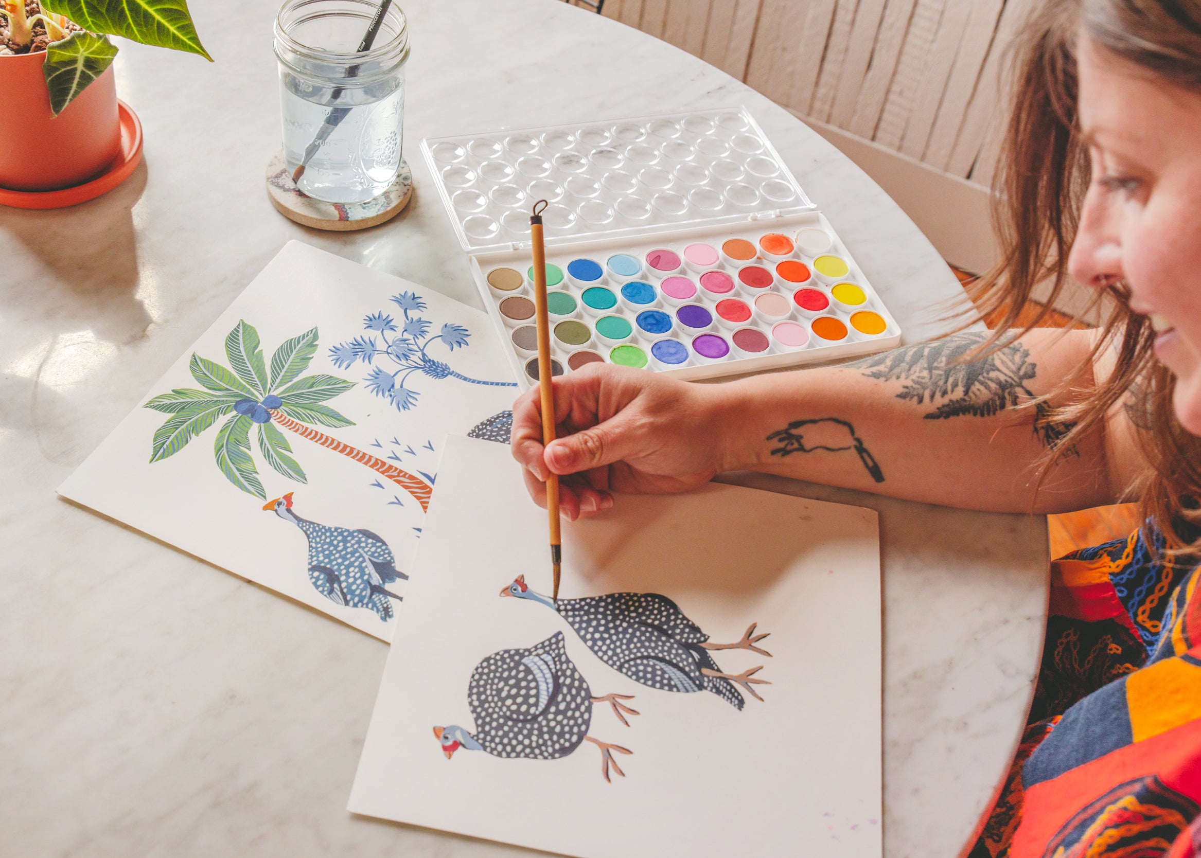 Person painting guinea fowl and tropical plant illustrations