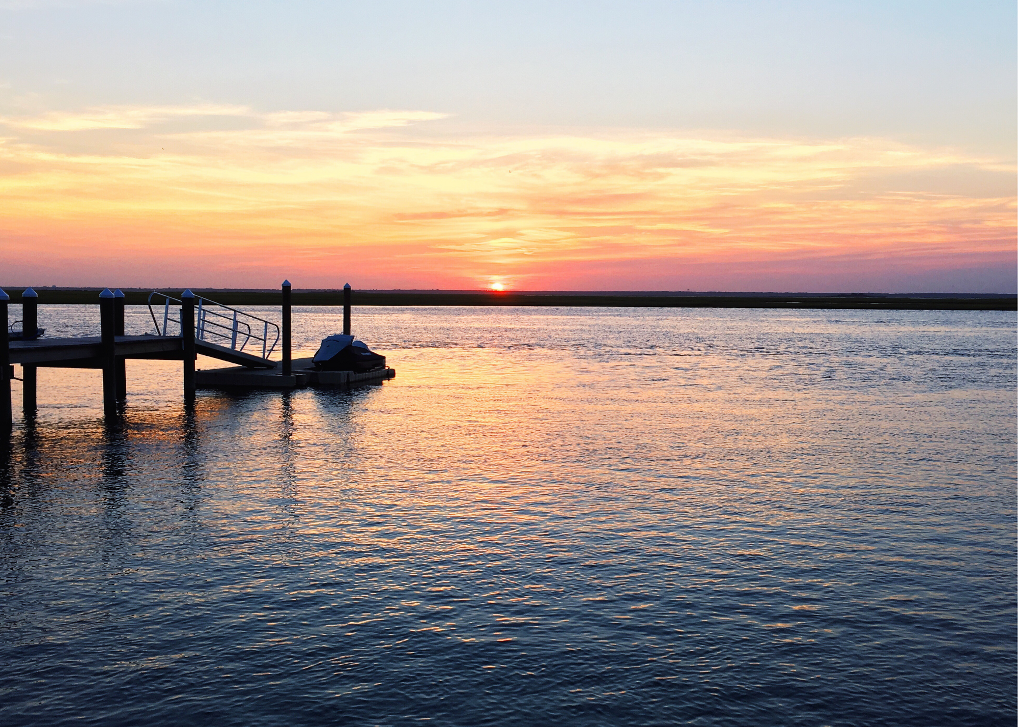 Sunset over calm water with a silhouetted dock and floating platform.