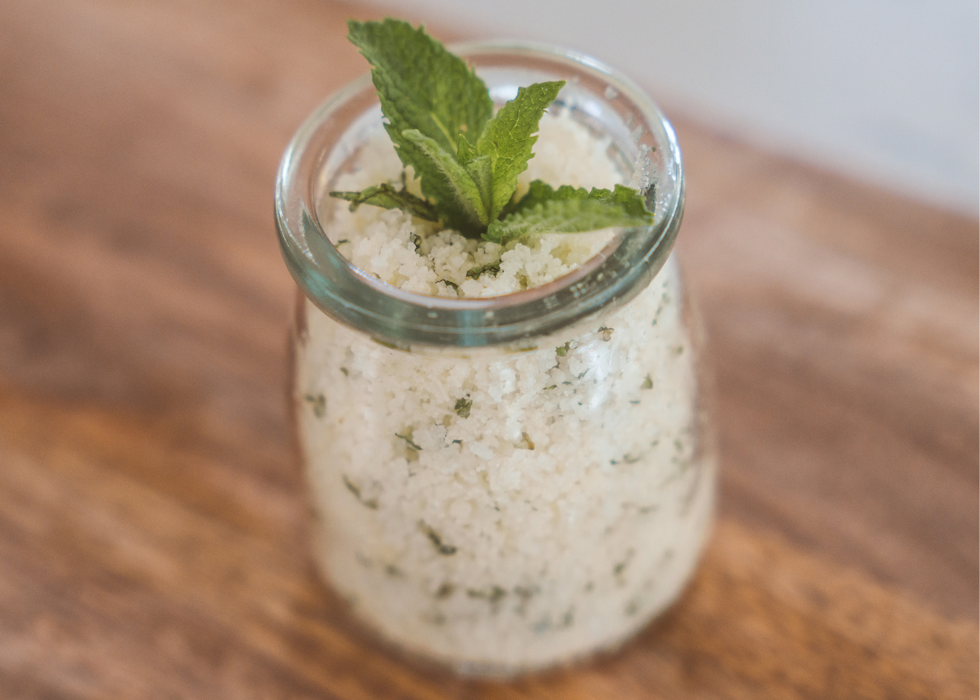 Glass jar filled with white crystals and mint flecks, topped with fresh mint leaves.