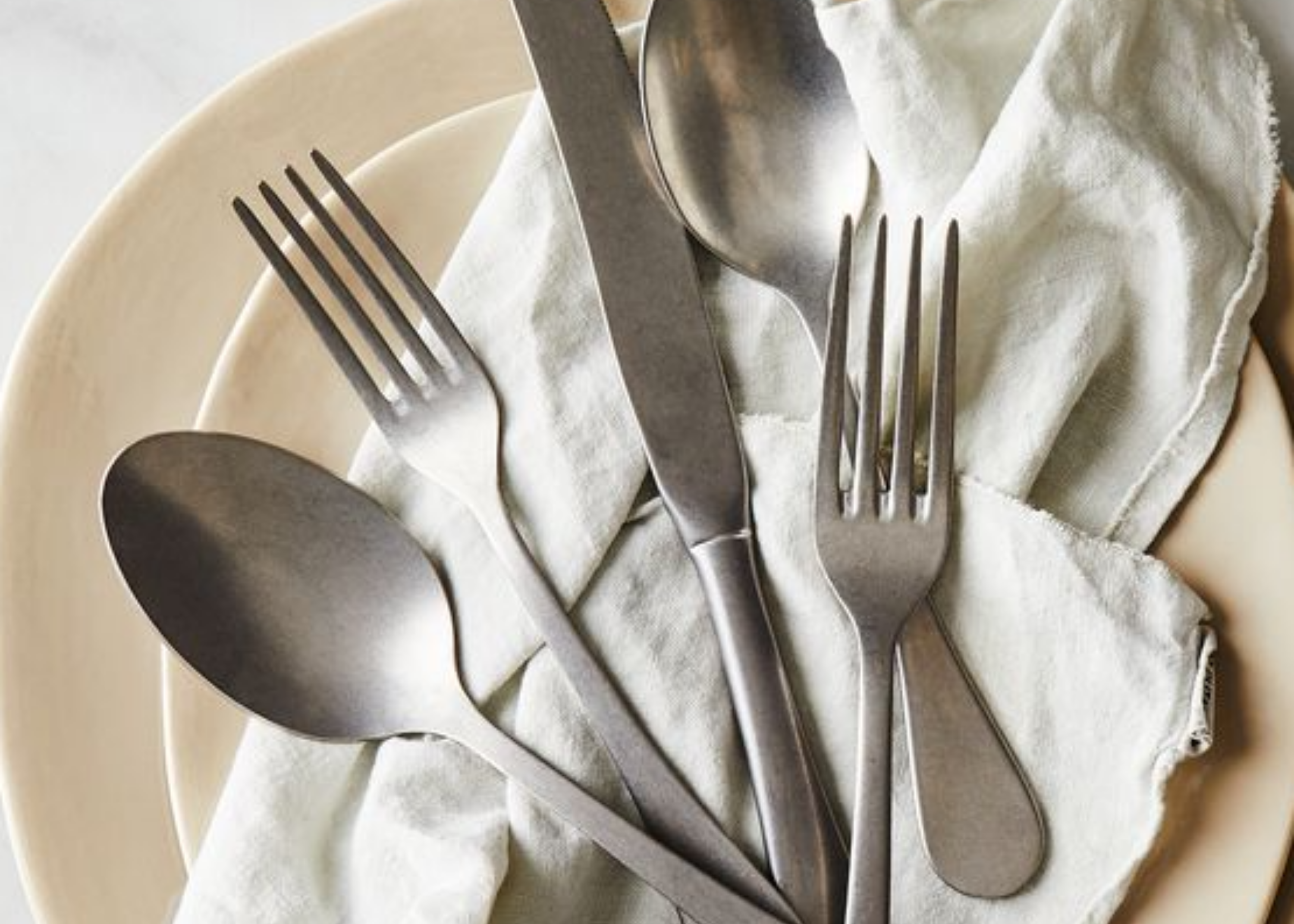 Assorted forks, spoons, and knives arranged on a white napkin inside a plate.