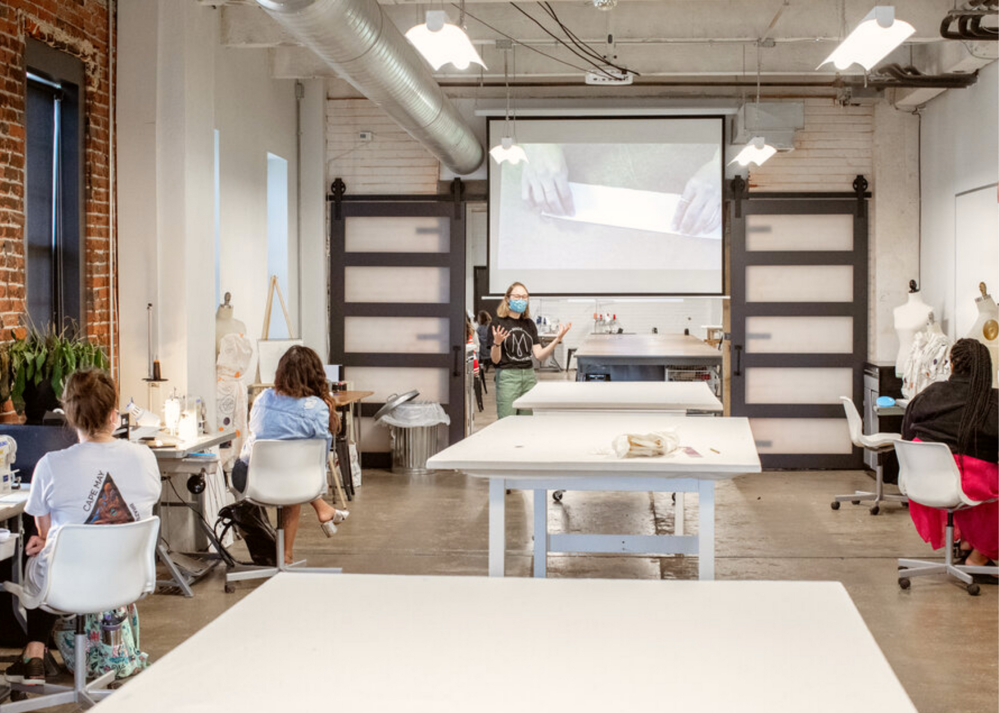 People working at tables in a fashion design studio as a presenter stands before a projection screen