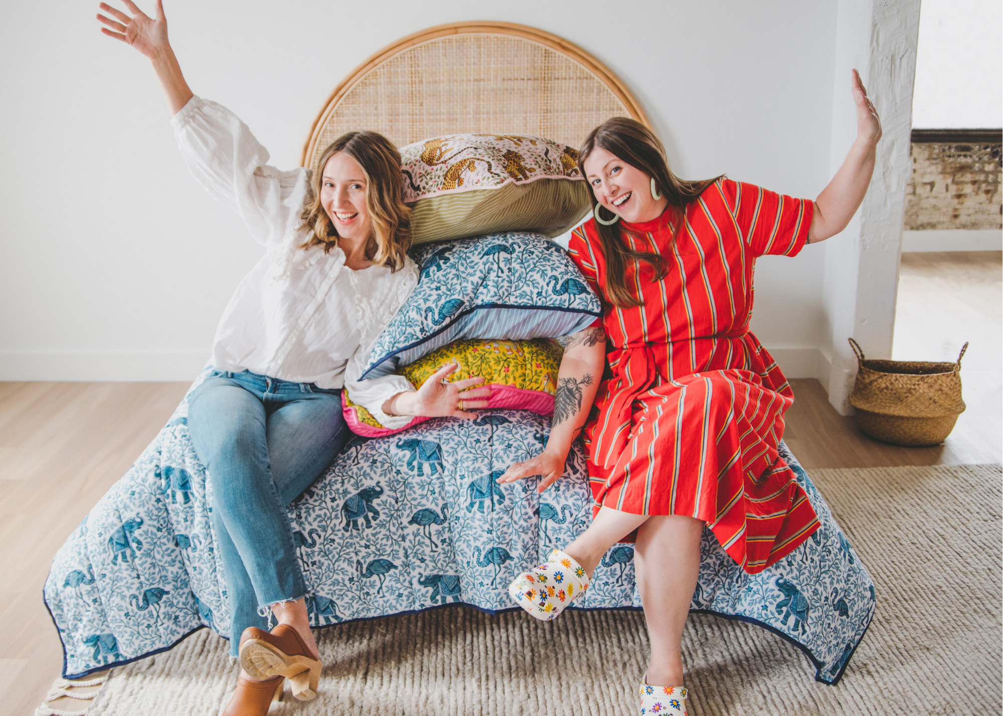 Two people seated on a bed surrounded by patterned pillows