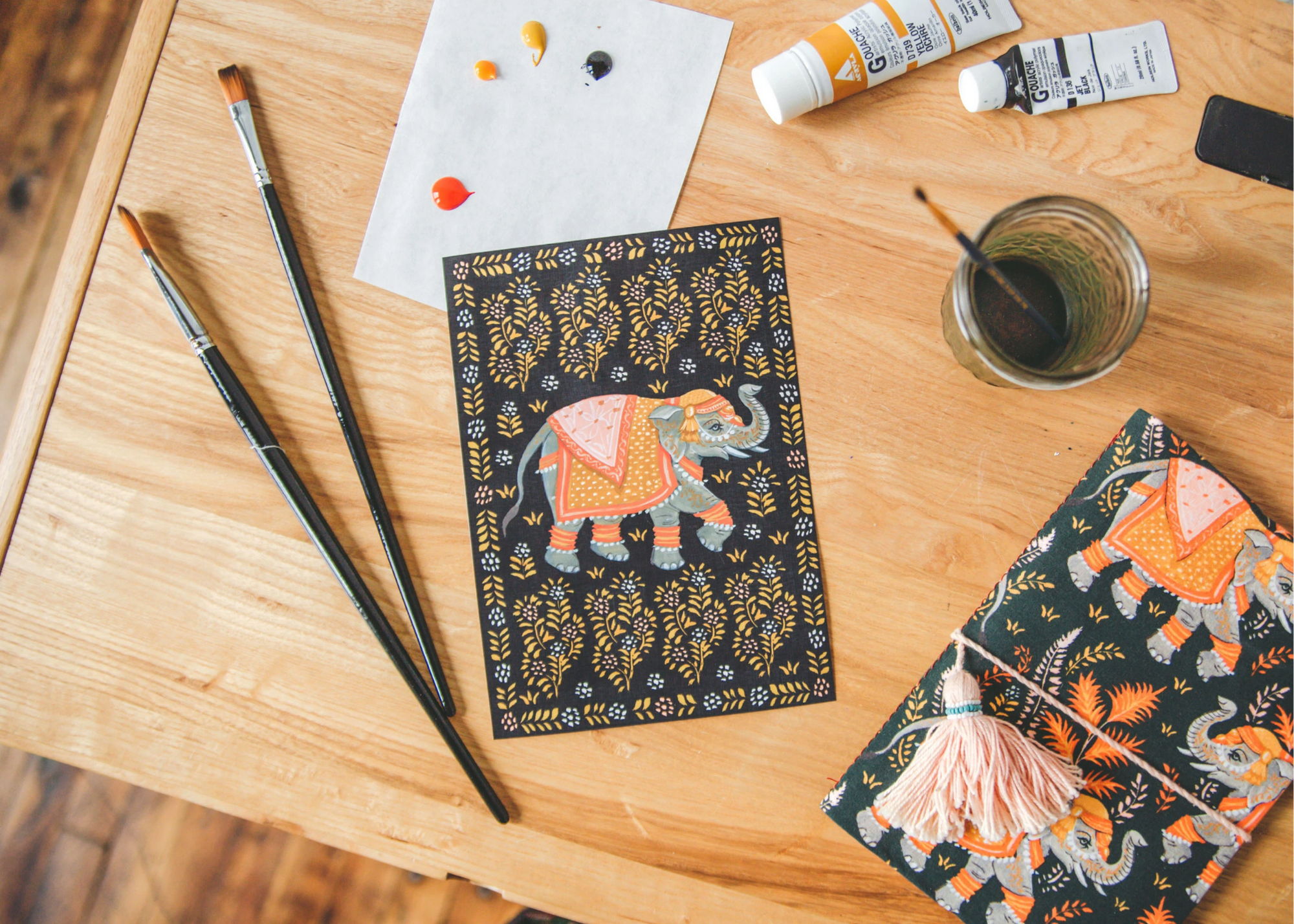 Painting supplies and elephant-patterned artwork arranged on a wooden table.