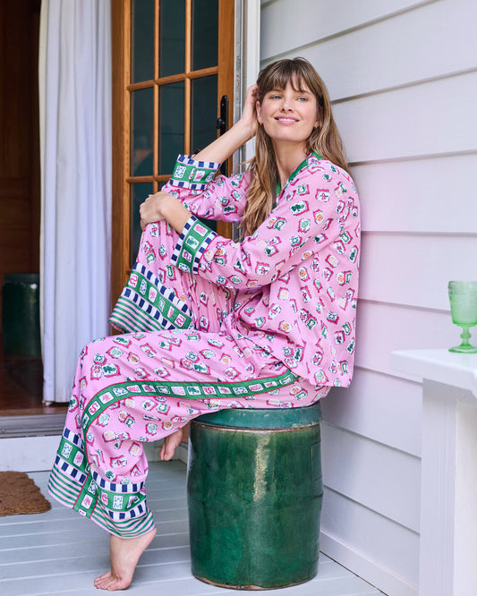 Peony Pink Lucky Tiles long pajama set shown while seated, with contrasting cuffs, side borders, and wide-leg hems.