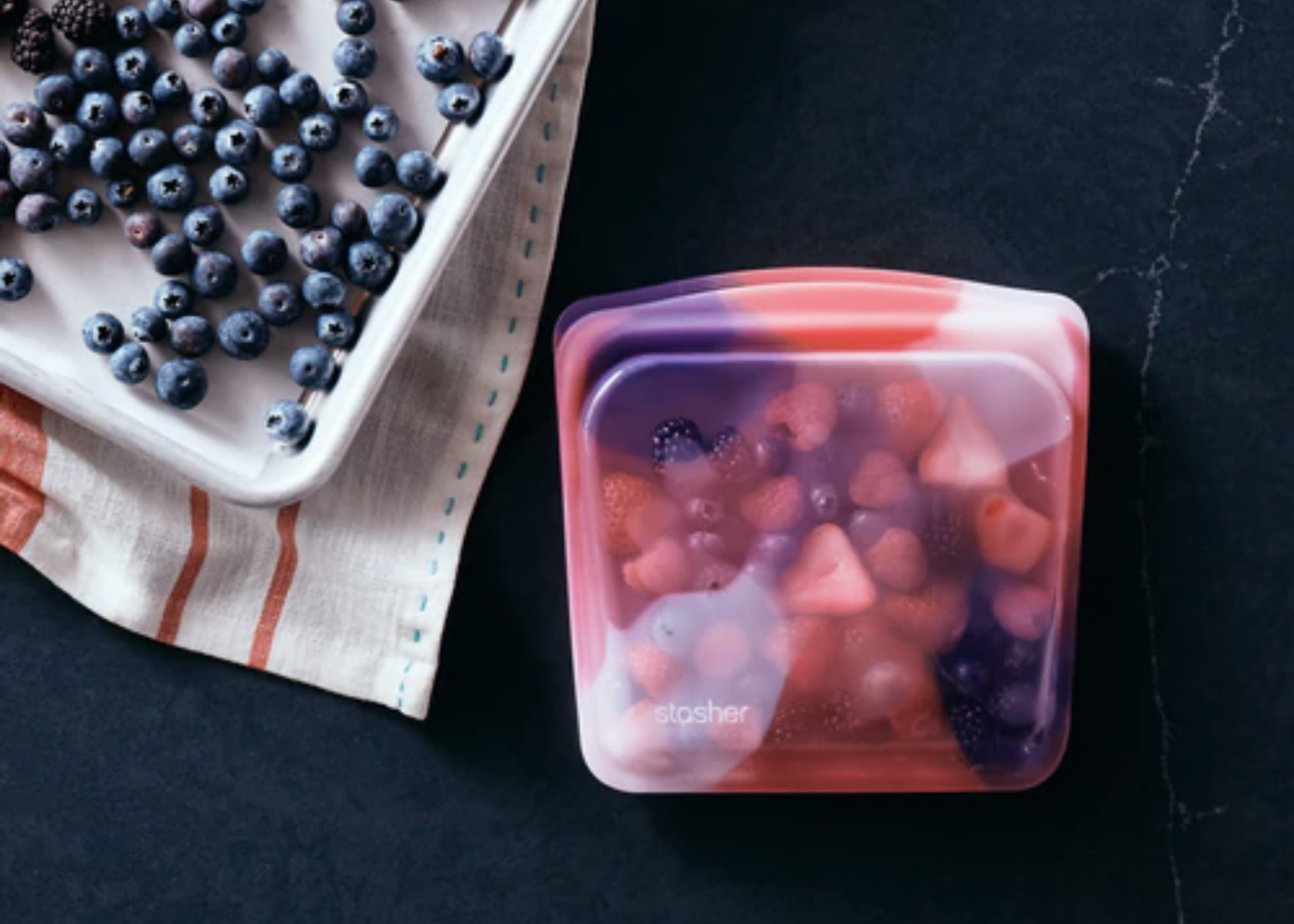 Blueberries on a tray beside a translucent reusable bag filled with mixed berries.