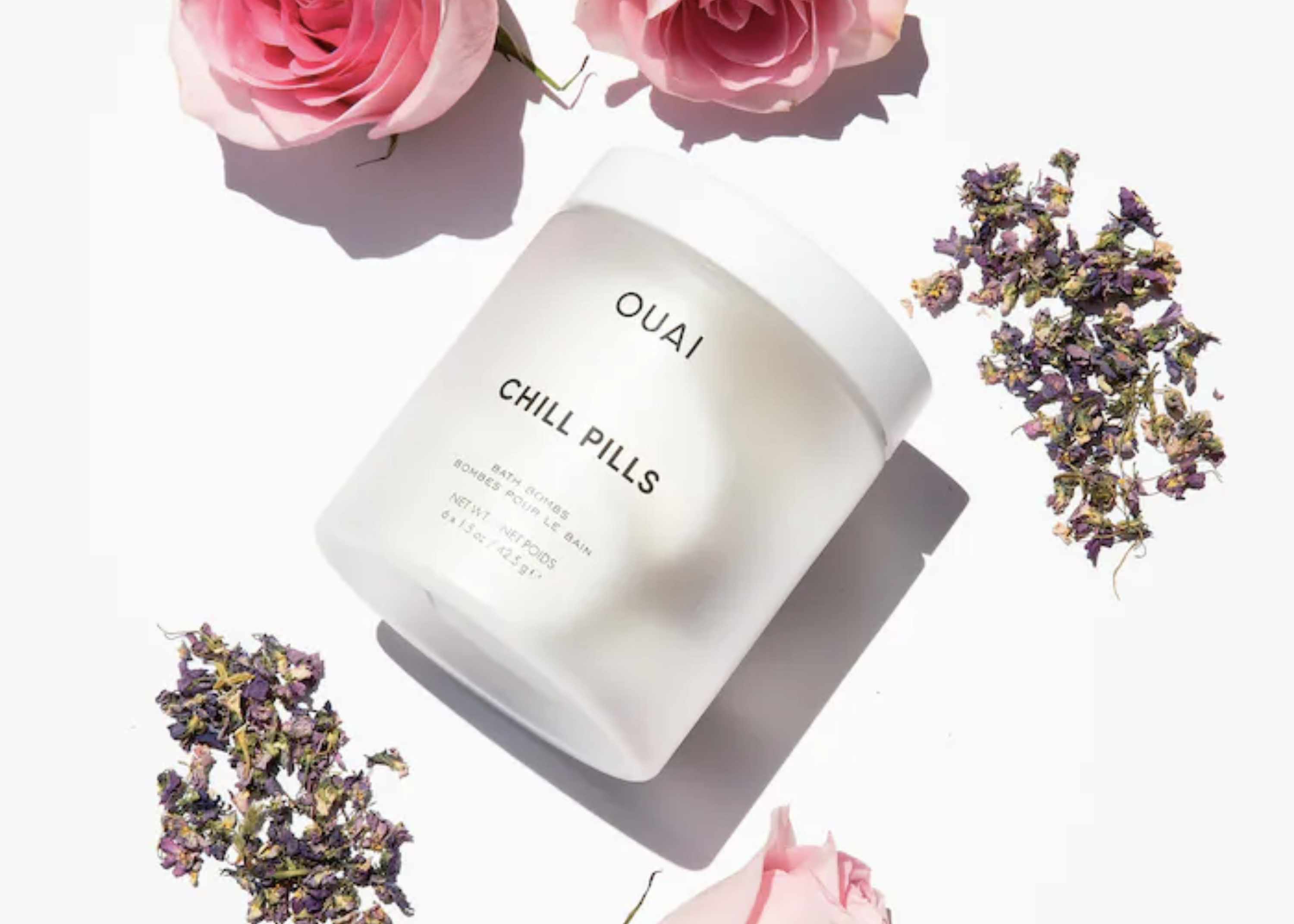 White OUAI Chill Pills jar surrounded by pink roses and dried purple flowers.