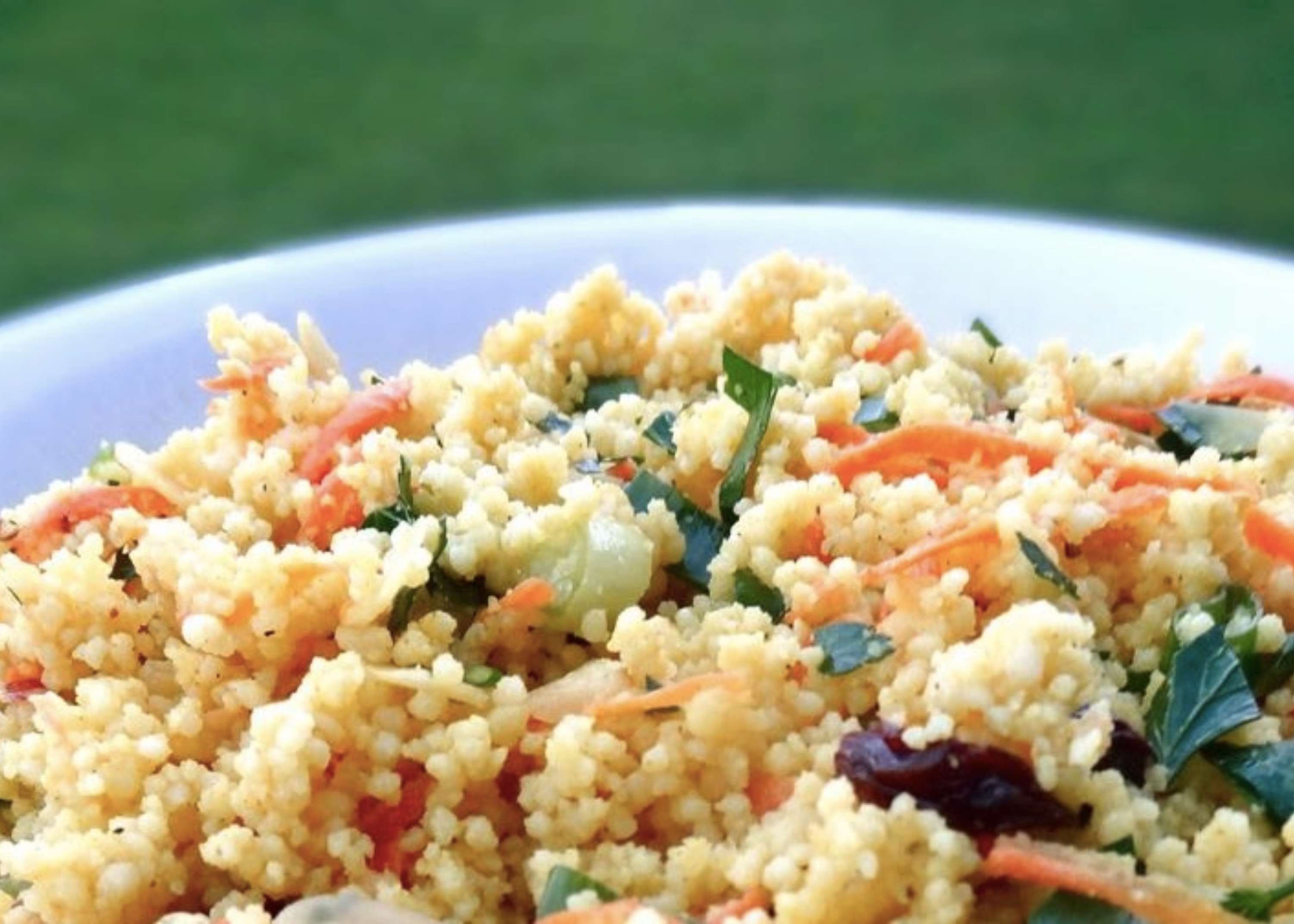 Close-up of a grain dish mixed with vegetables and herbs on a plate.