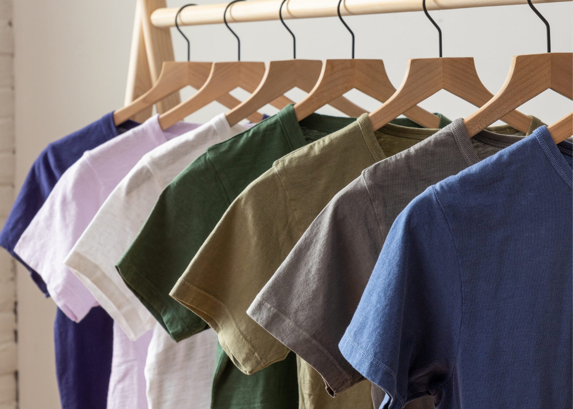 Short-sleeved shirts in blue, gray, khaki, green, white, lavender, and dark blue hanging on wooden hangers.