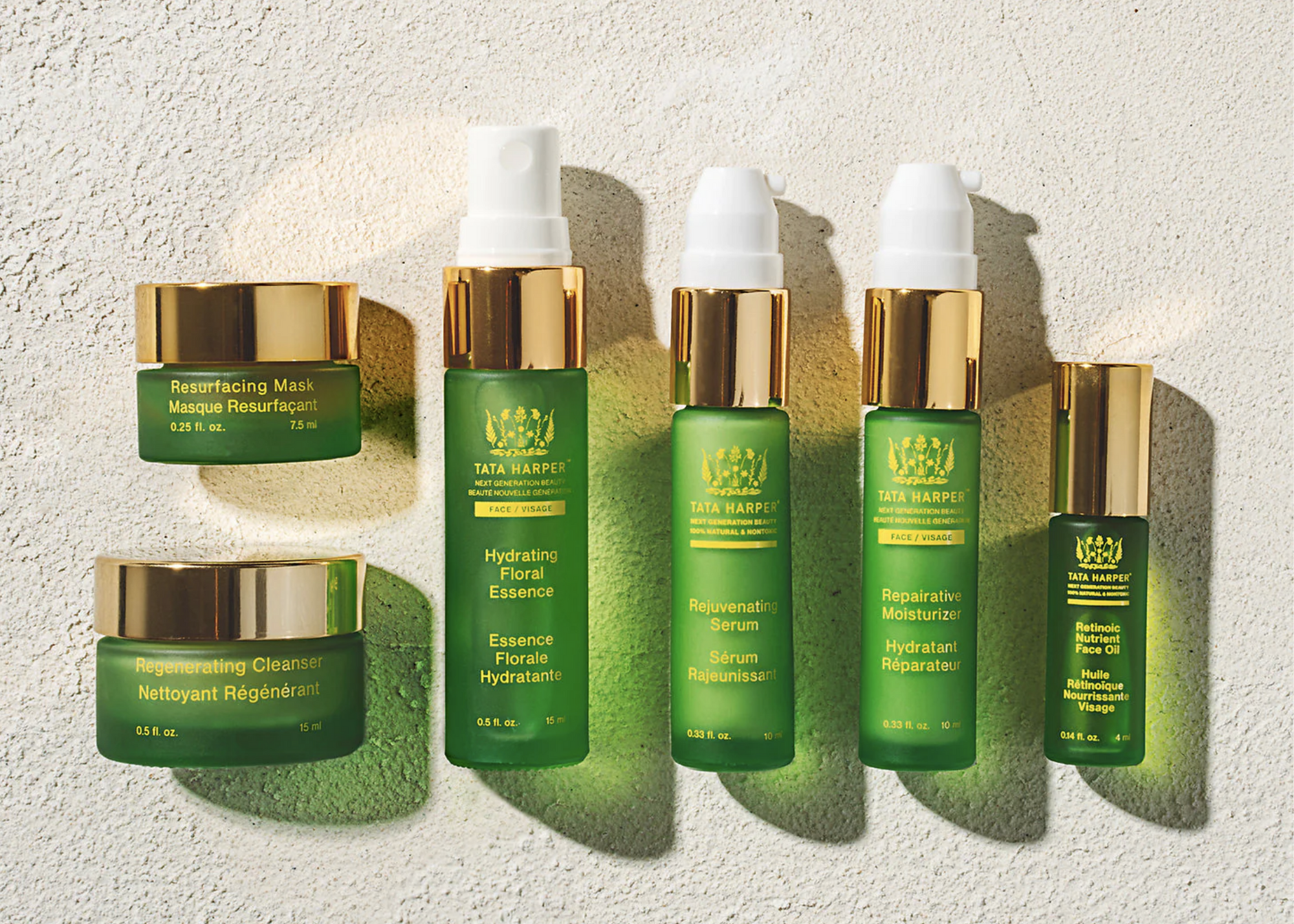 Green Tata Harper skincare products with gold caps arranged against a textured wall.