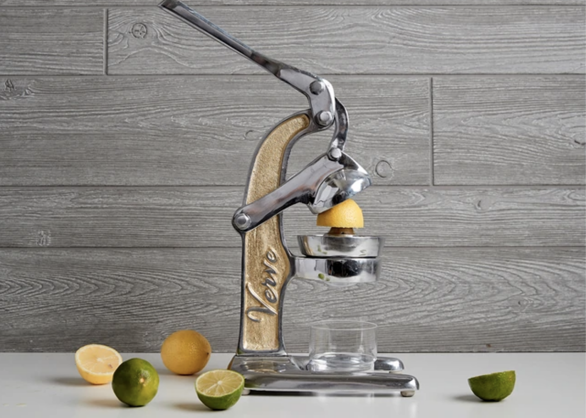 Metal citrus press over a glass with lemons and limes