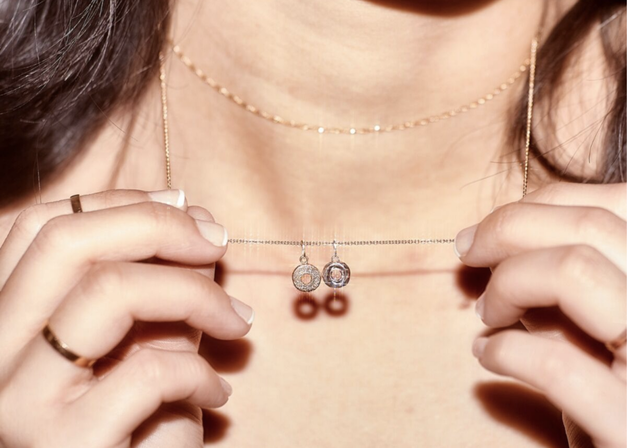 Close-up of a person holding two delicate necklaces with round pendants.