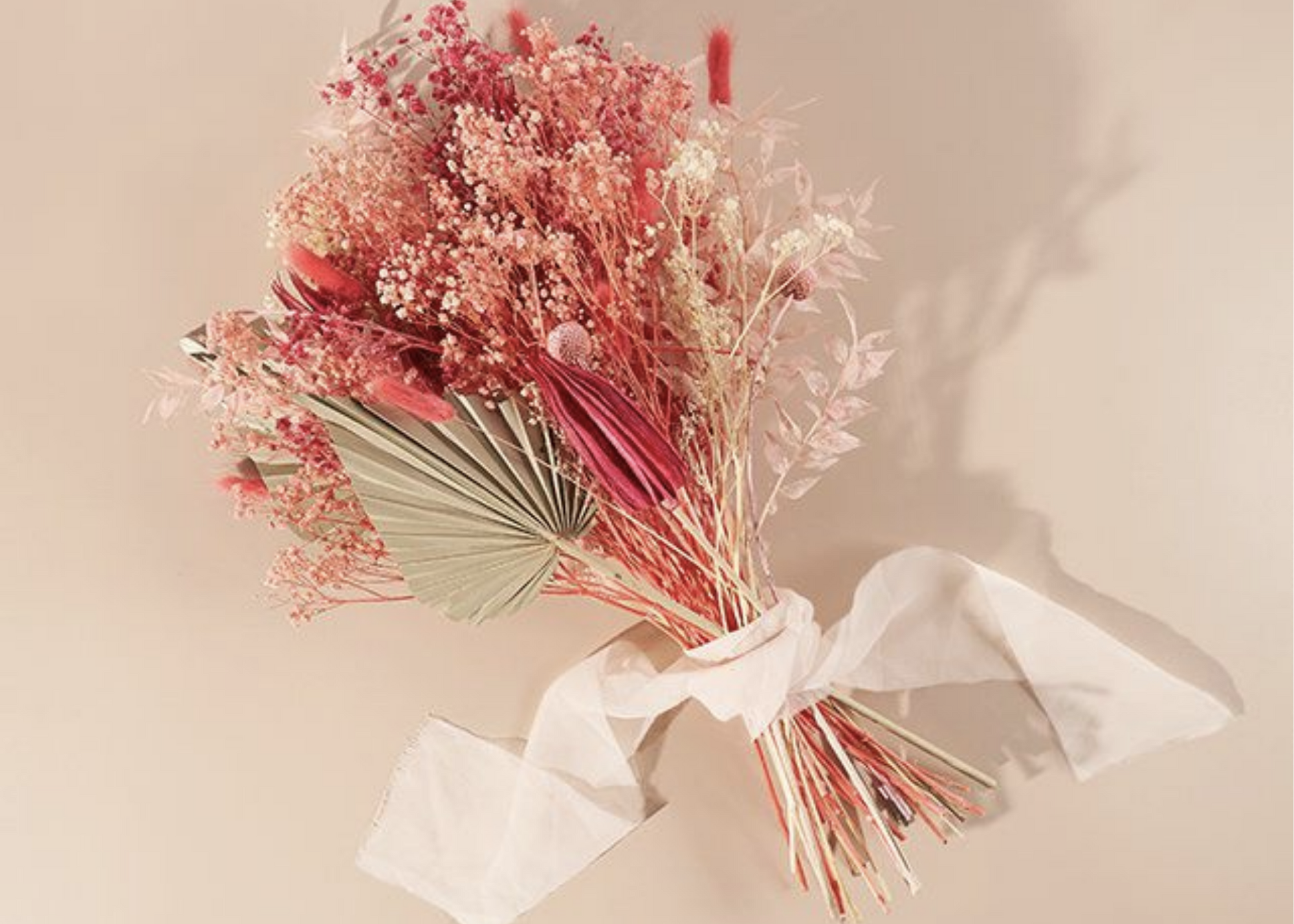 Pink and cream dried flower bouquet tied with a white ribbon.