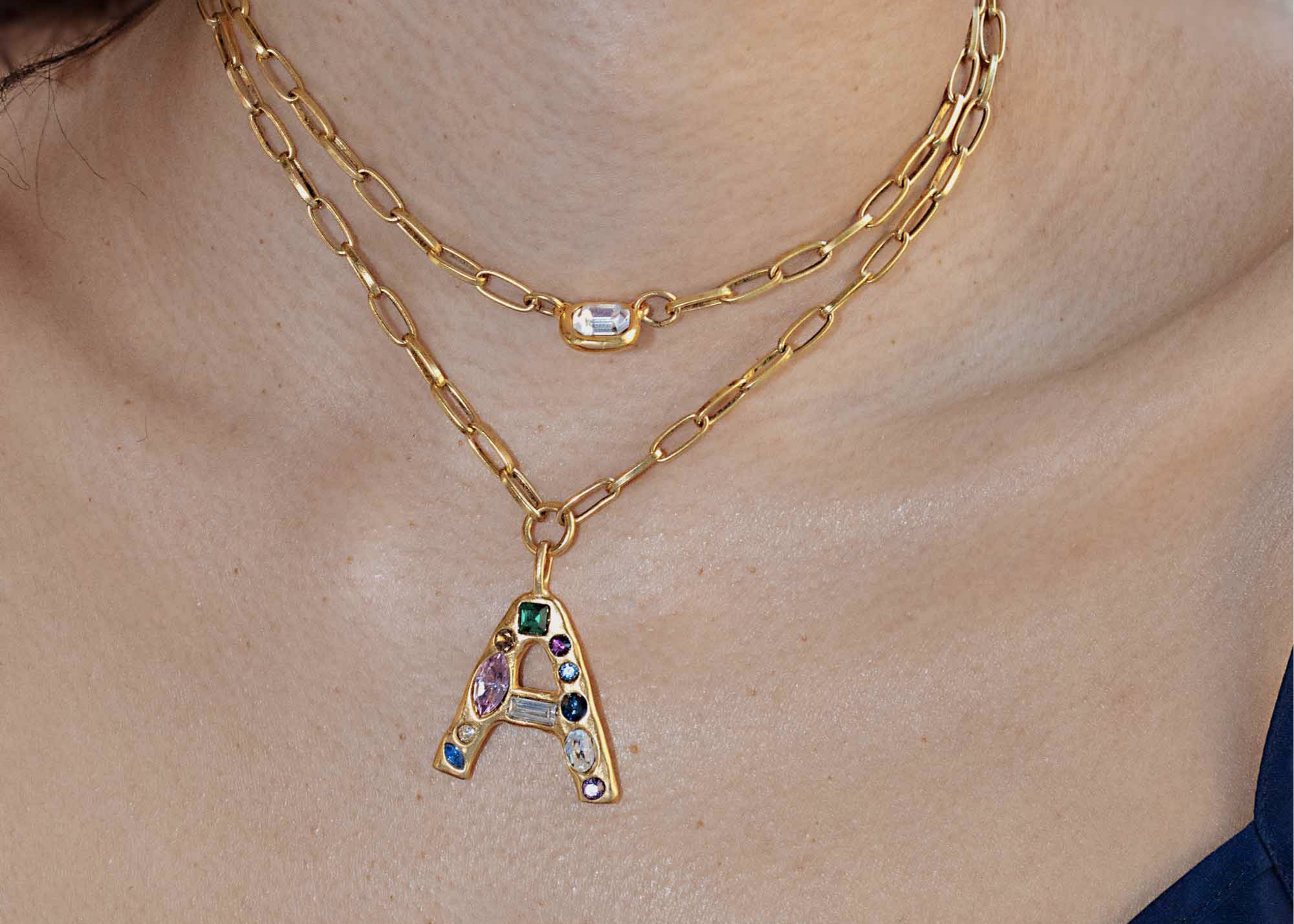 Layered gold necklaces with a jeweled letter A pendant.