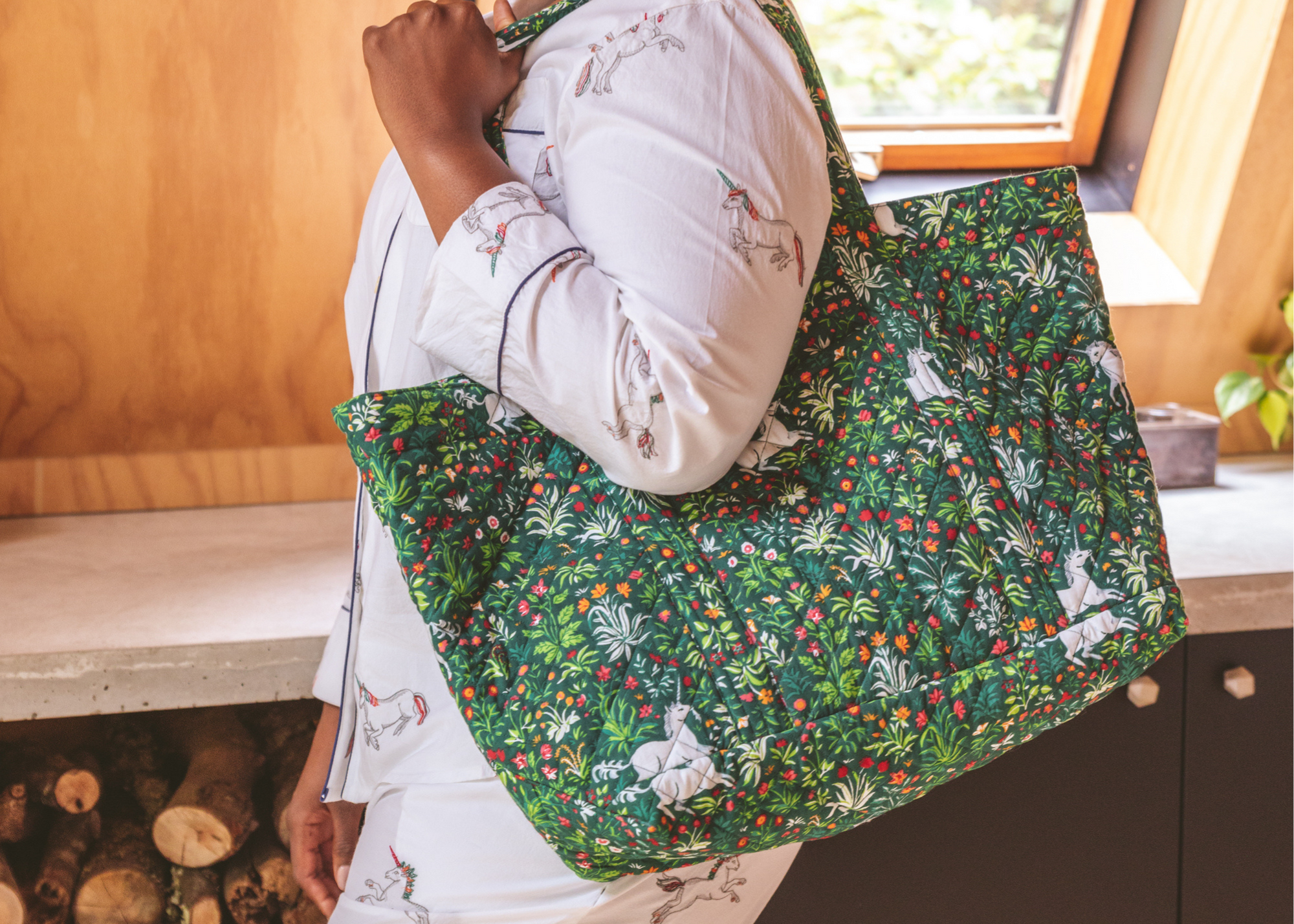 Person carrying a large green floral tote bag indoors.