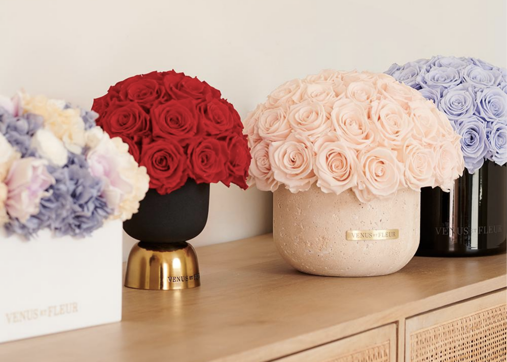 Red, pale pink, lavender, and mixed flower arrangements in vases on a wooden cabinet.
