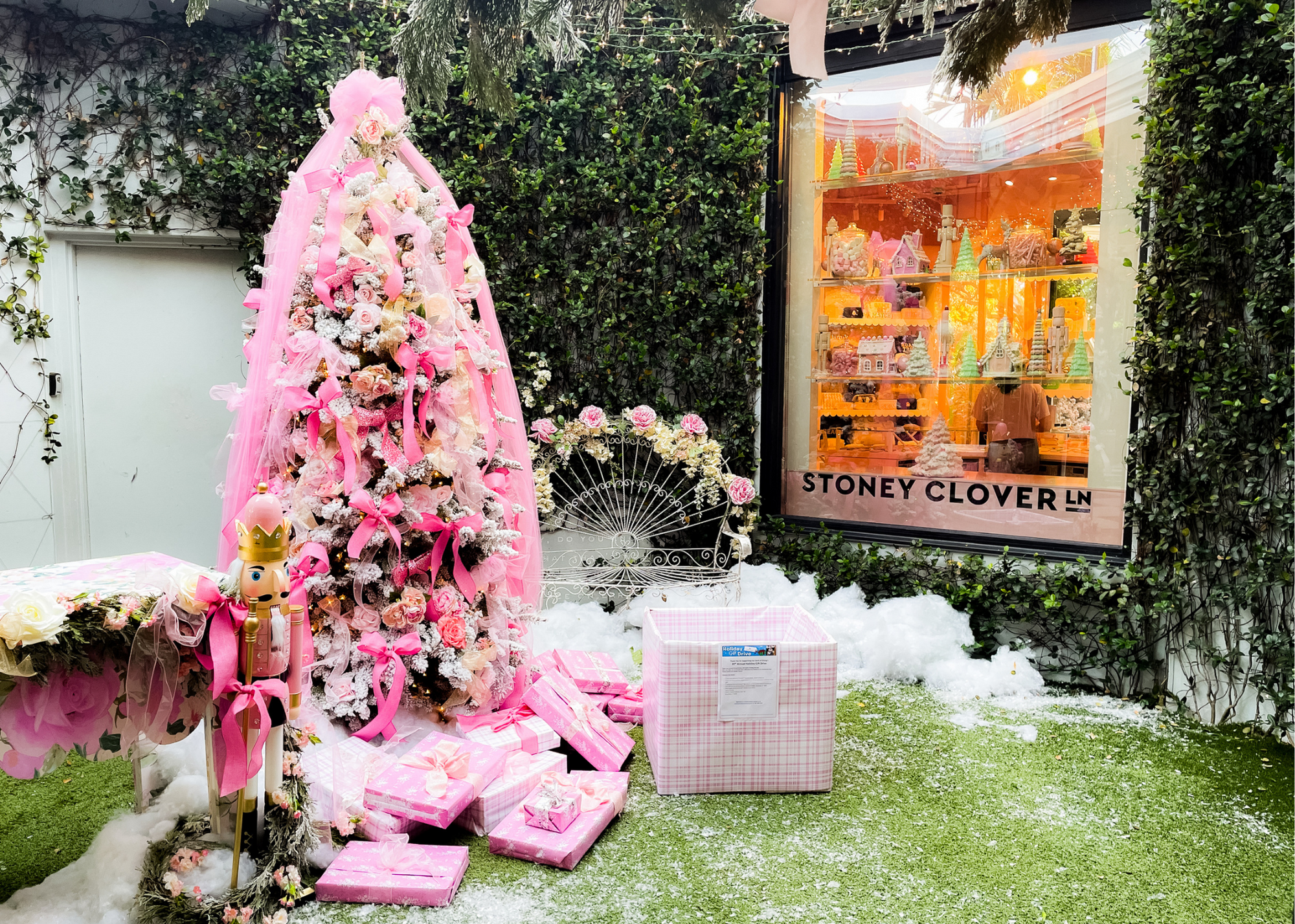 Pink decorated Christmas tree and wrapped gifts outside a display window labeled STONEY CLOVER LN.