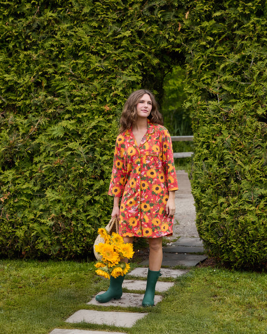 Person wearing an orange floral sleep shirt with three-quarter sleeves, standing outdoors and holding a basket of sunflowers.