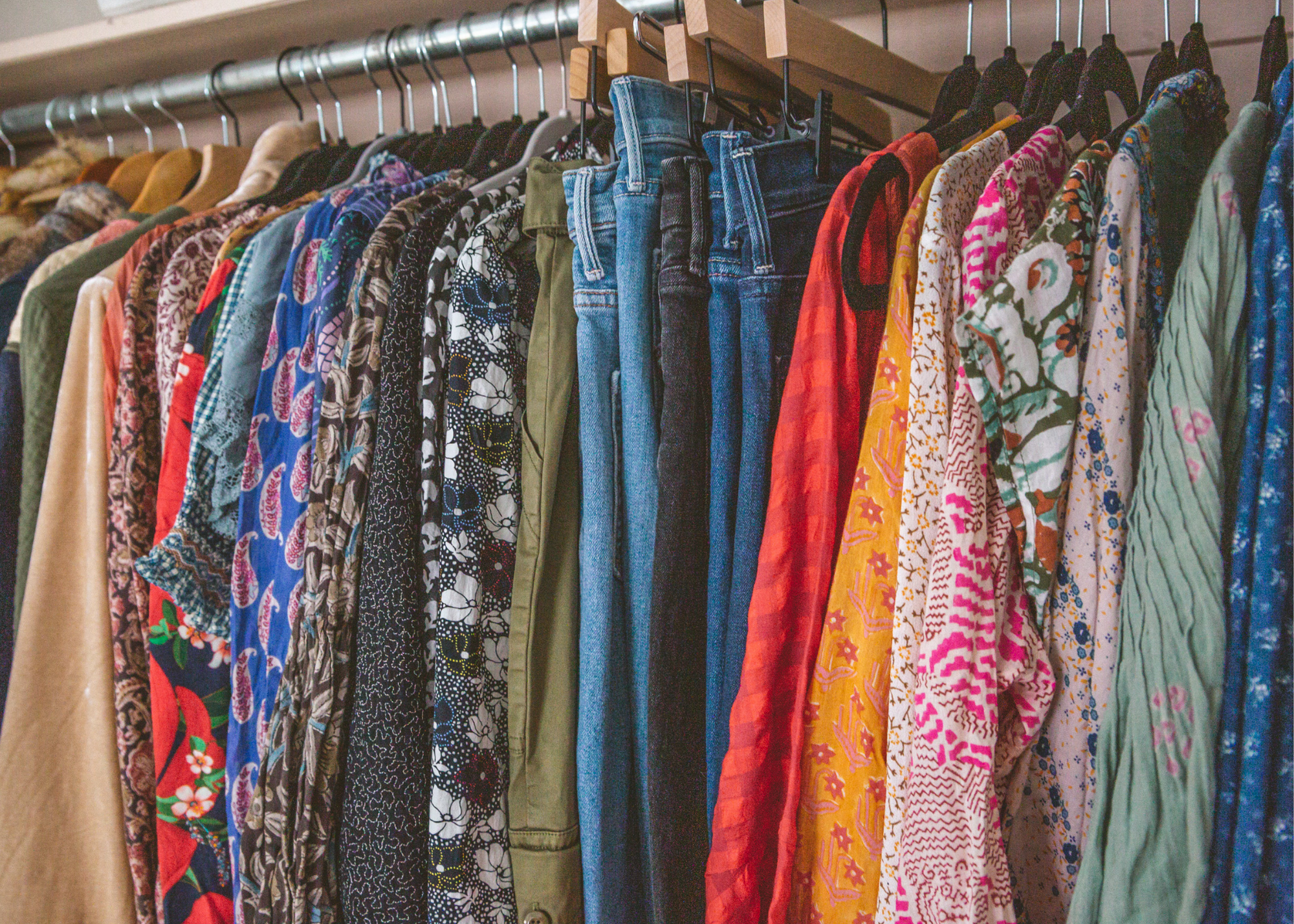 Clothing rack filled with assorted patterned garments, jackets, trousers, and jeans.