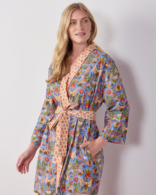 Person wearing the Delphinium Blue Bee Tapestry robe, showing its floral and bee print, shawl collar, matching belt, and pockets.