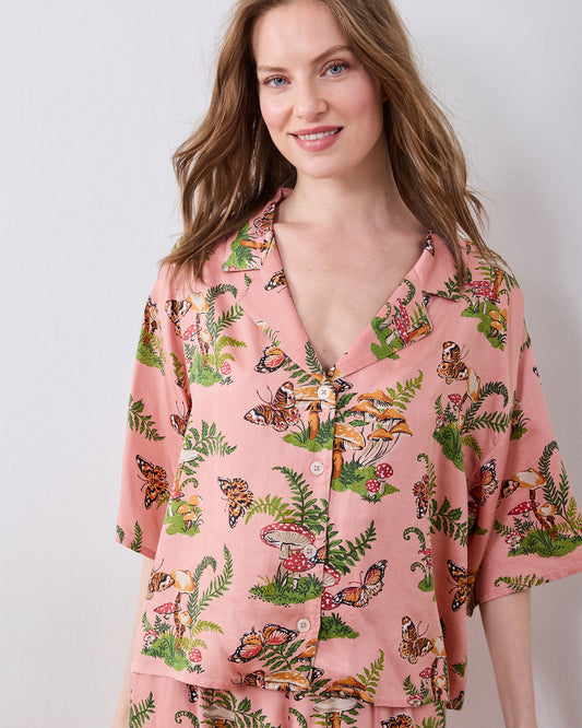 Close-up of a rosewood pajama top with a butterfly, mushroom, and fern print, showing its notched collar and button front.