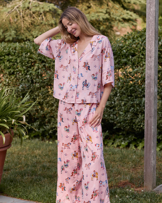 Model outdoors wearing the pink long pajama set with a horse-and-cowgirl print, cropped short-sleeved top, and wide-leg pants.