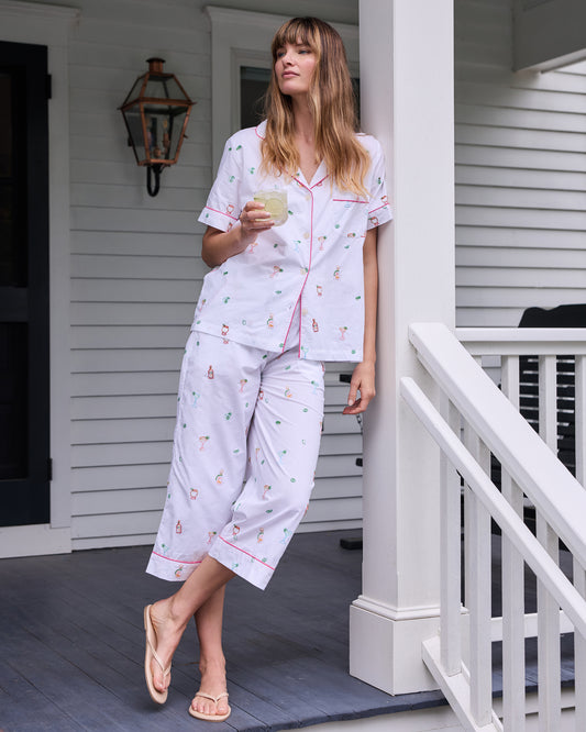 Person wearing the cloud short-sleeve pajama top and cropped pants with embroidered cocktail-themed motifs while holding a glass on a porch.