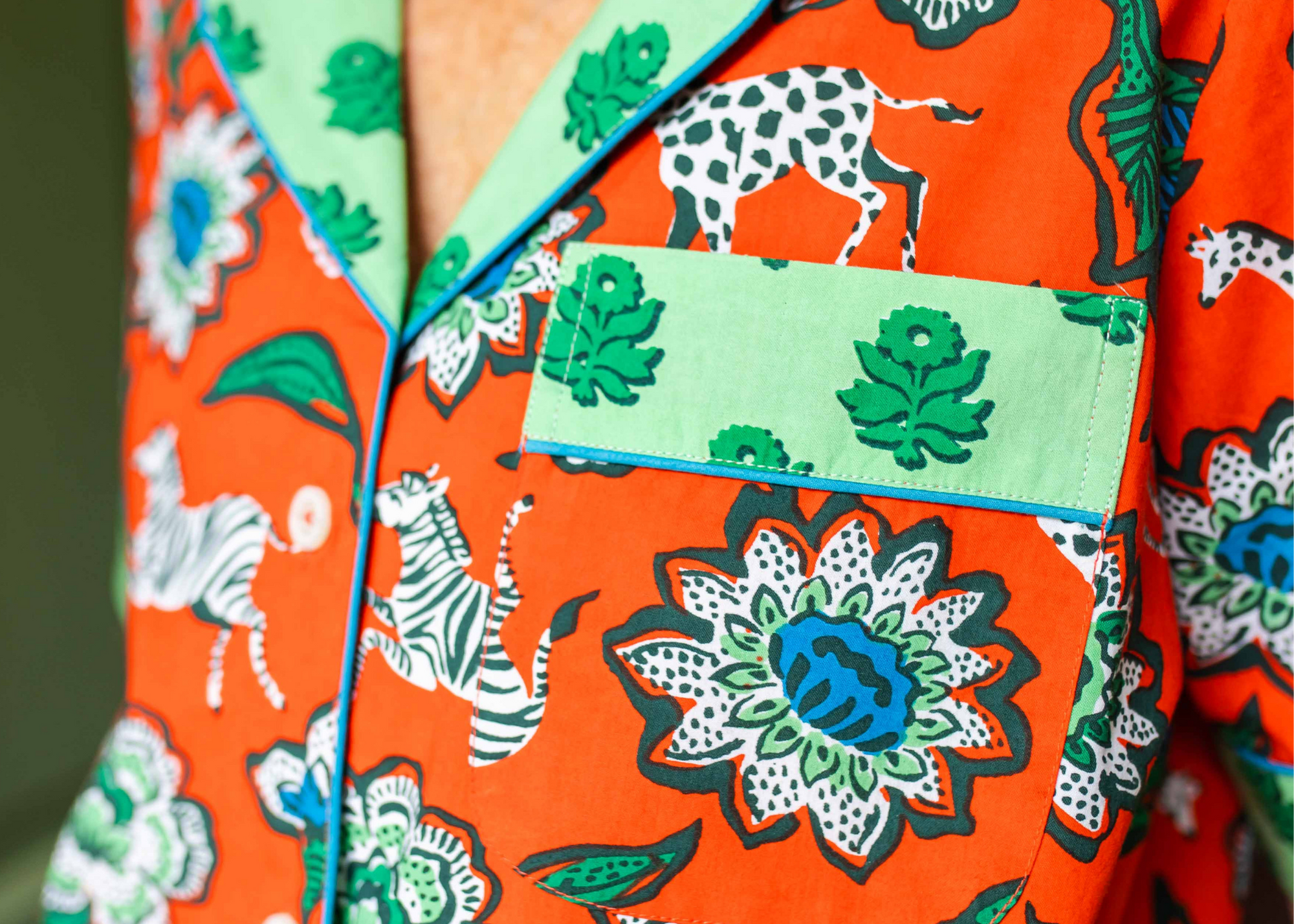Close-up of a bright orange patterned garment with flowers, zebras, and a green flap pocket.