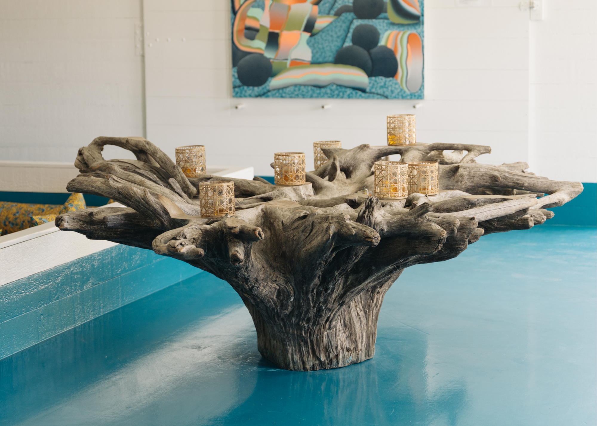 Driftwood table with small candle holders in a bright room overlooking blue water.