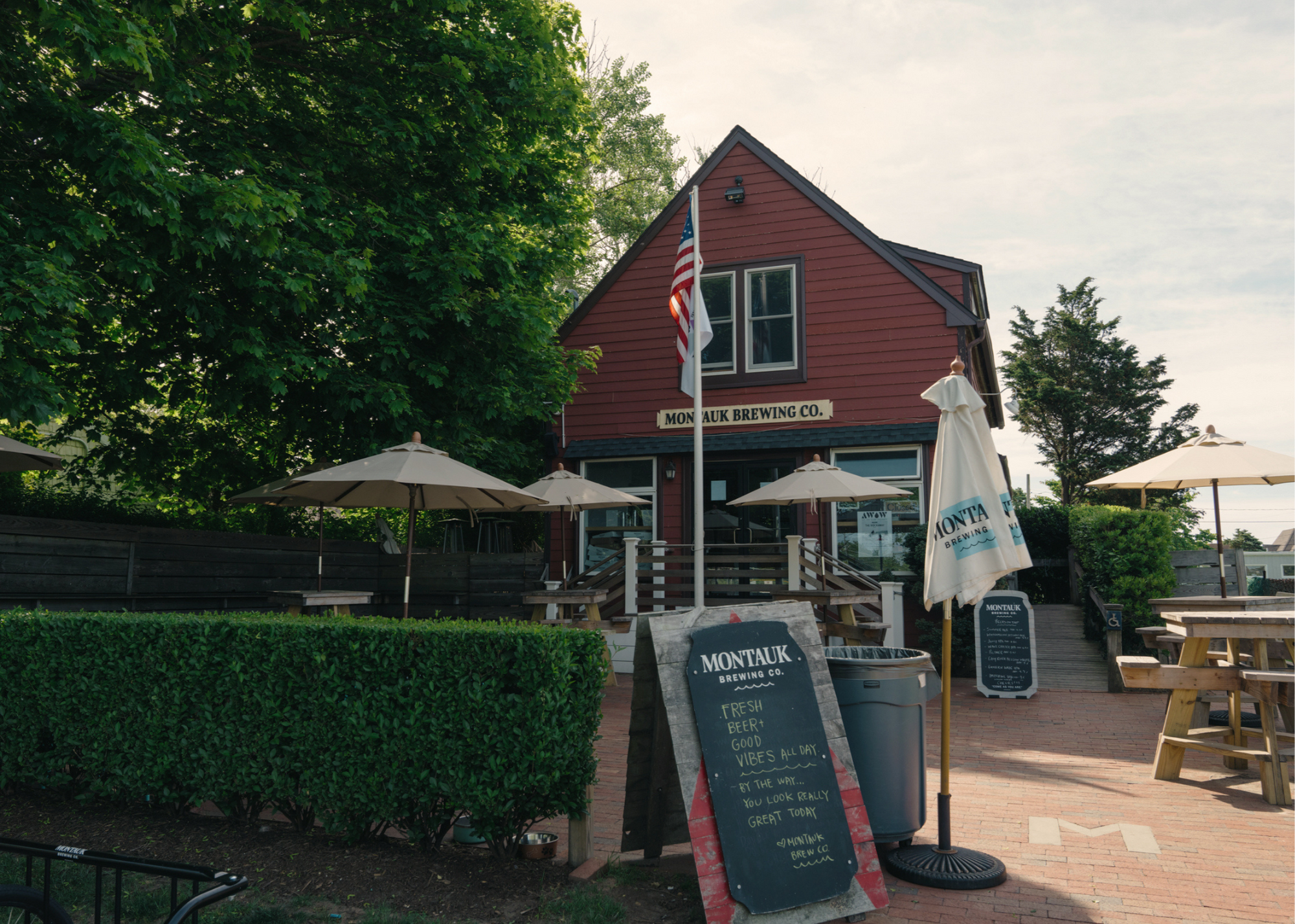 Red Montauk Brewing Co. building with outdoor umbrellas, picnic tables, and a chalkboard sign.