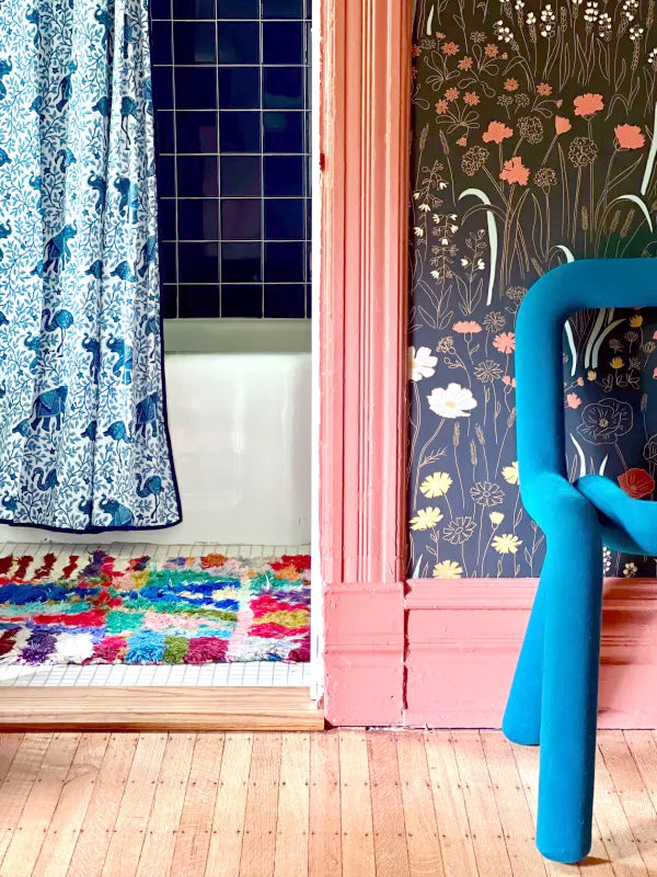 Colorful bathroom interior with a blue-and-white patterned shower curtain, tiled wall, multicolored rug, pink trim, and a blue curved object
